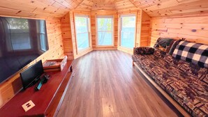 Interior acolhedor de uma cabana com paredes de madeira, uma televisão grande, um sofá e piso de madeira.