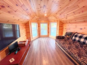 Een gezellig cabin interieur met houten wanden, een grote televisie, een bank en een houten vloer.