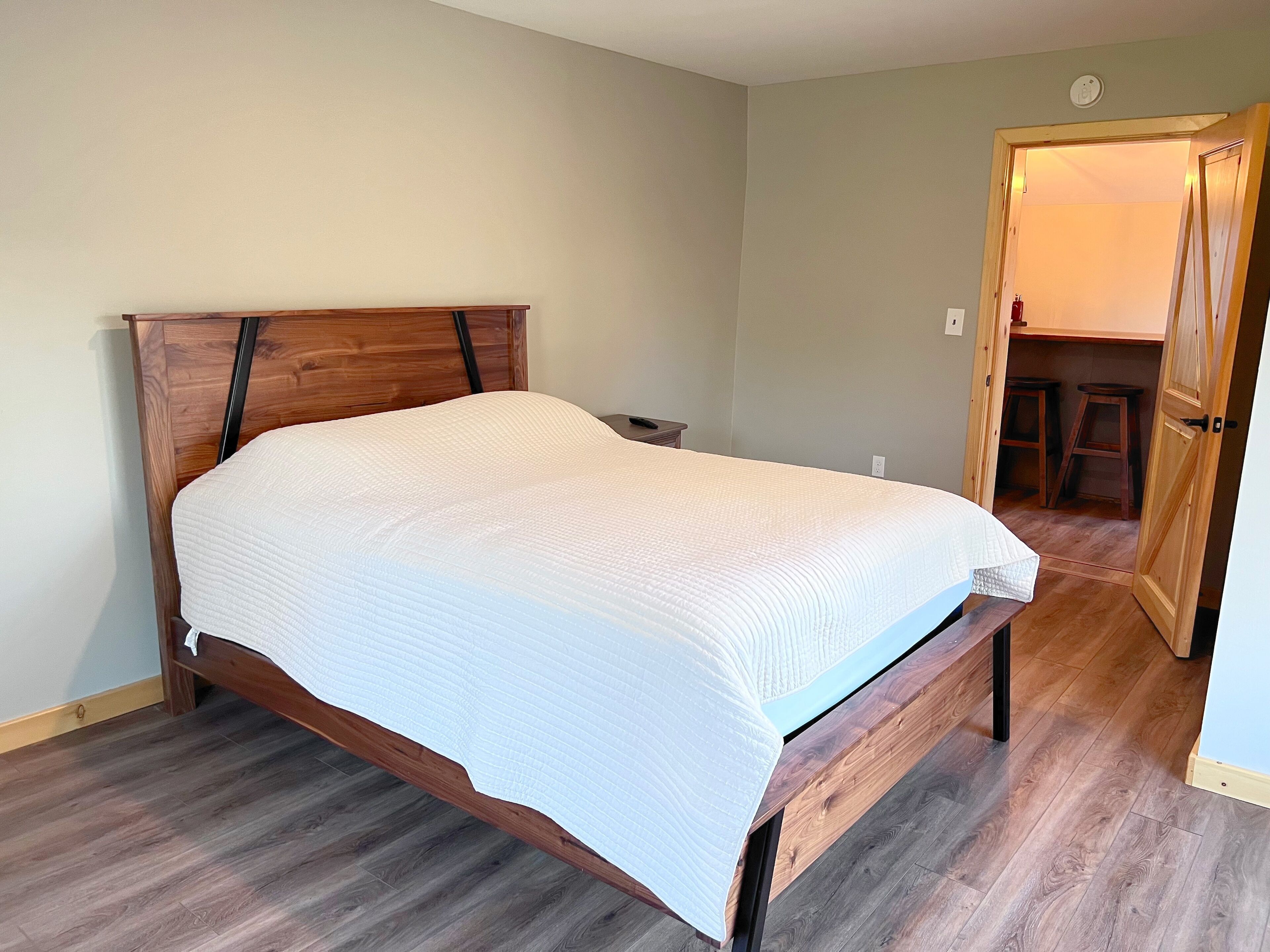 A bedroom with a wooden bed frame, a white bedspread, and a wooden floor.