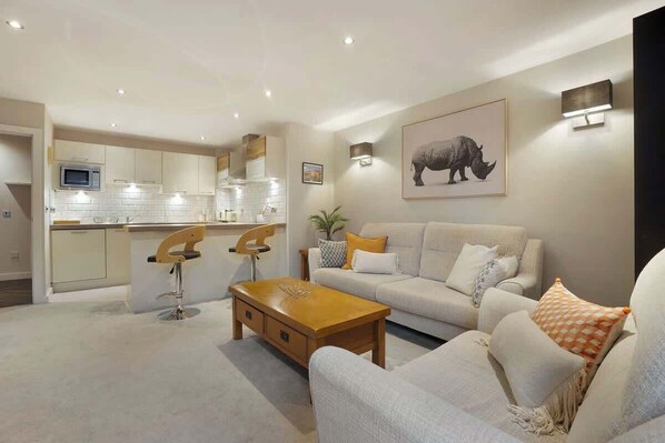 A modern living room with a sofa, coffee table, and a kitchen area with a microwave.