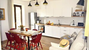 A modern kitchen with white cabinets, a dining table with red chairs, and a sofa with a hat. - Beautiful cottage a few miles from Bellagio with stunning views of Lake Como (Civenna di Bellagio)