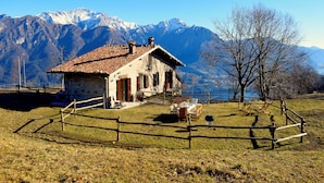 A rustic chalet with a tiled roof, surrounded by a wooden fence, set against a backdrop of snow-capped mountains. - Beautiful cottage a few miles from Bellagio with stunning views of Lake Como (Civenna di Bellagio)
