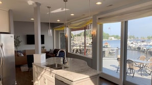 A modern kitchen with a large island, a built-in dishwasher, and a view of a marina through large windows.
