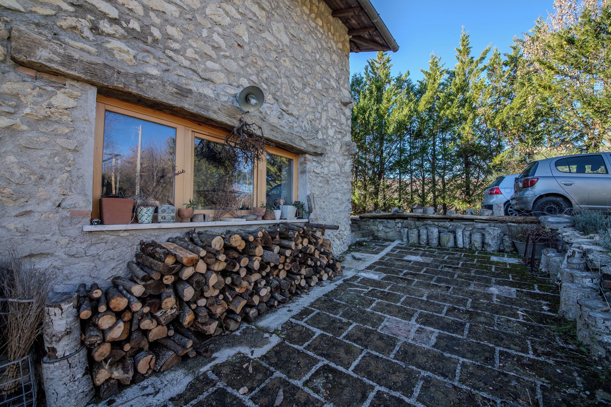 A stone building with a window, a stack of firewood, and a parked car.