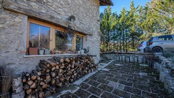 A stone building with a window, a stack of firewood, and a parked car.