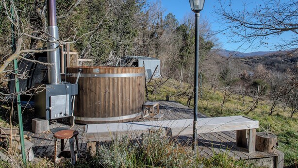 Eine rustikale Holzsauna im Freien mit einem Metallbrenner und einer Holzdielen-Terrasse.