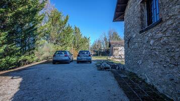 A gravel driveway with two parked cars, a stone building with a window, and a wooden structure in the background.