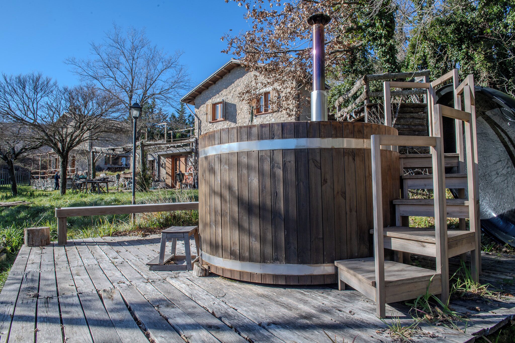 Un bain à remous en bois, doté d’une cheminée en métal, d’escaliers en bois et d’une terrasse en bois.