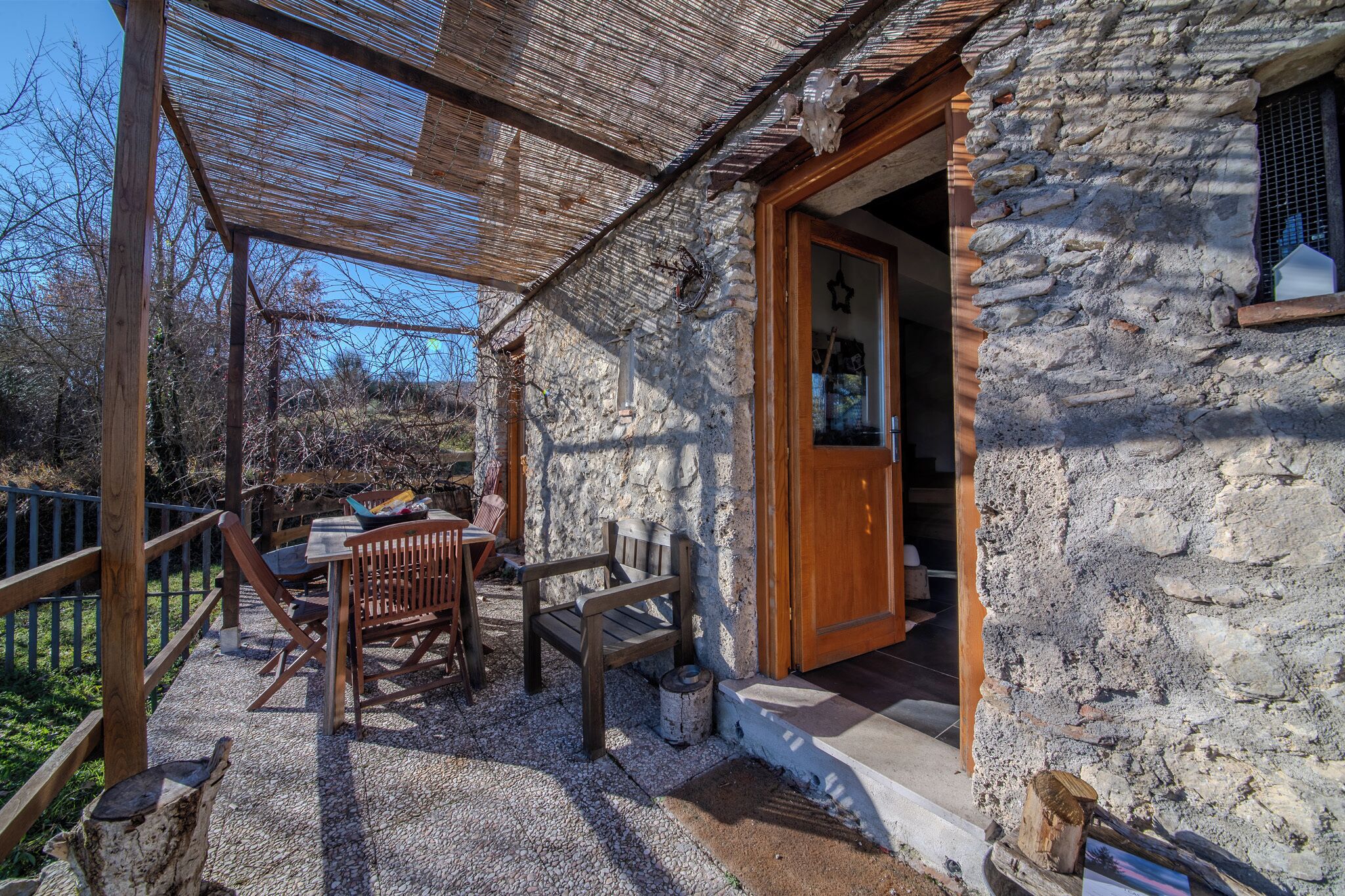 A stone building with a wooden door and a covered outdoor seating area with a table and chairs.