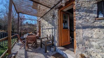 A stone building with a wooden door and a covered outdoor seating area with a table and chairs.
