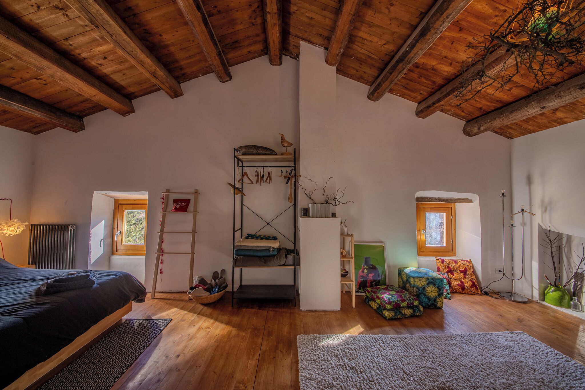 Un dormitorio acogedor en un ático con techo de madera, camas literas, una escalera, un radiador, una ventana y una pequeña silla verde.