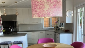 Een moderne keuken met witte kastjes, een centraal eiland en een eetgedeelte met een ronde houten tafel en roze stoelen.