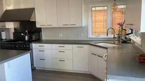 Een moderne keuken met witte kasten, een rvs-fornuis en een raam met houten zonwering.