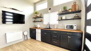 A modern kitchen with black cabinets, a wooden countertop, a microwave, and a window with blinds. - The Whole Property to Yourself - 3 Cozy Elk Riverfront Tiny Cabins at High Bank (Noel)