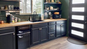 A modern kitchen with dark cabinetry, a wooden countertop, and a large window. - The Whole Property to Yourself - 3 Cozy Elk Riverfront Tiny Cabins at High Bank (Noel)