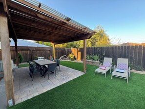 Une terrasse couverte avec une table et des chaises, une pelouse et une clôture en bois en arrière-plan.