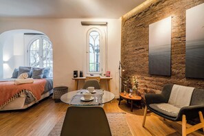 Ein gemütliches Zimmer mit einem Bett, einem Esstisch mit Stühlen, einem Sofa und einem großen Fenster.