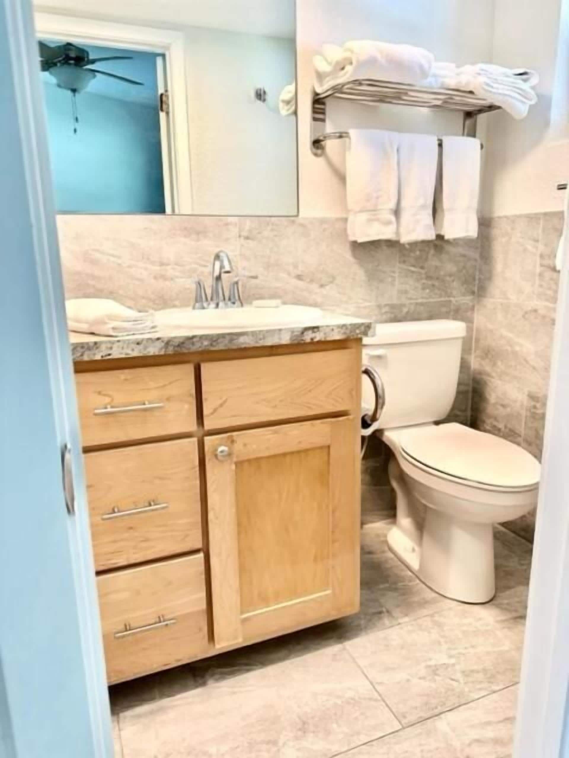 A bathroom with a marble sink, wooden cabinets, a toilet, and a towel rack.