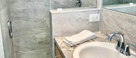 Un baño moderno con cabina de ducha de vidrio, zona de ducha con azulejos de mármol, lavamanos con encimera de mármol y un espejo grande.