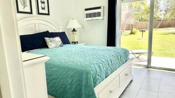 A bedroom with a bed, a nightstand, a lamp, and a window with a view of a garden.