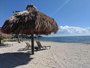 A beach with a thatched umbrella, lounge chairs, and a clear view of the ocean. - Matecumbe Resort (Islamorada)