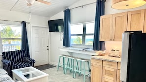 A compact kitchen with wooden cabinets, a refrigerator, and a window with curtains. - Matecumbe Resort (Islamorada)