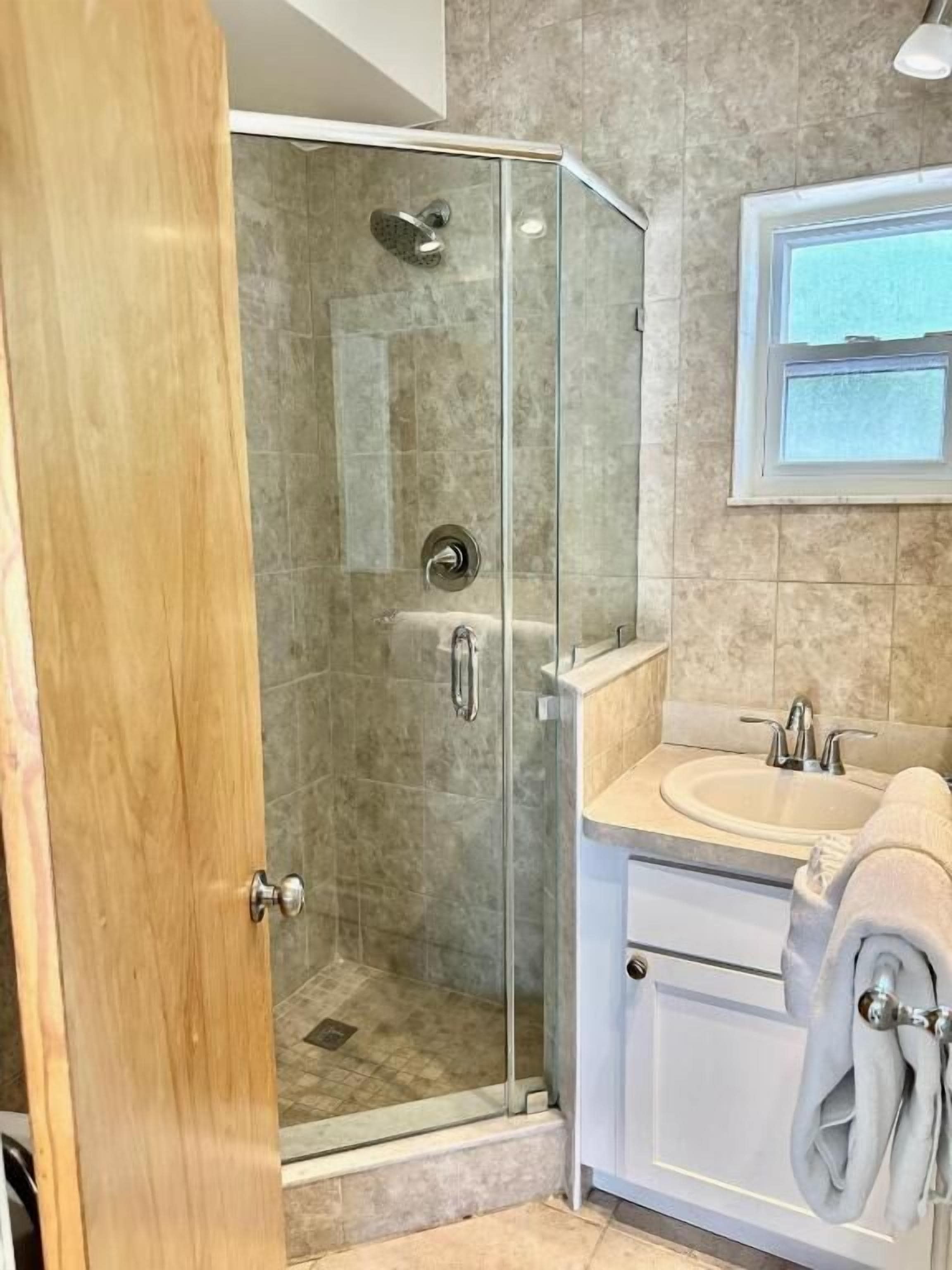 Un baño moderno con cabina de ducha de vidrio, un lavabo con espejo y un perchero con toallas.