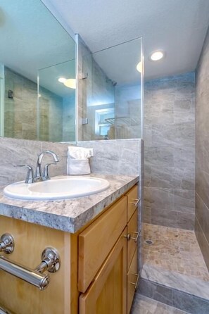 Un baño moderno con lavamanos de mármol, armarios de madera y cabina de ducha de vidrio.