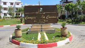 Une enseigne indiquant « Completo La Cassia Golf & Beach Resort », avec un jardin aménagé et des plantes en pot.