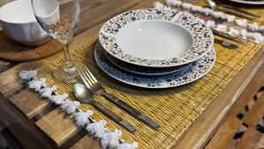 Une table à manger dressée avec des assiettes, un verre à vin et des couverts, le tout posé sur un set de table en fibres tressées.