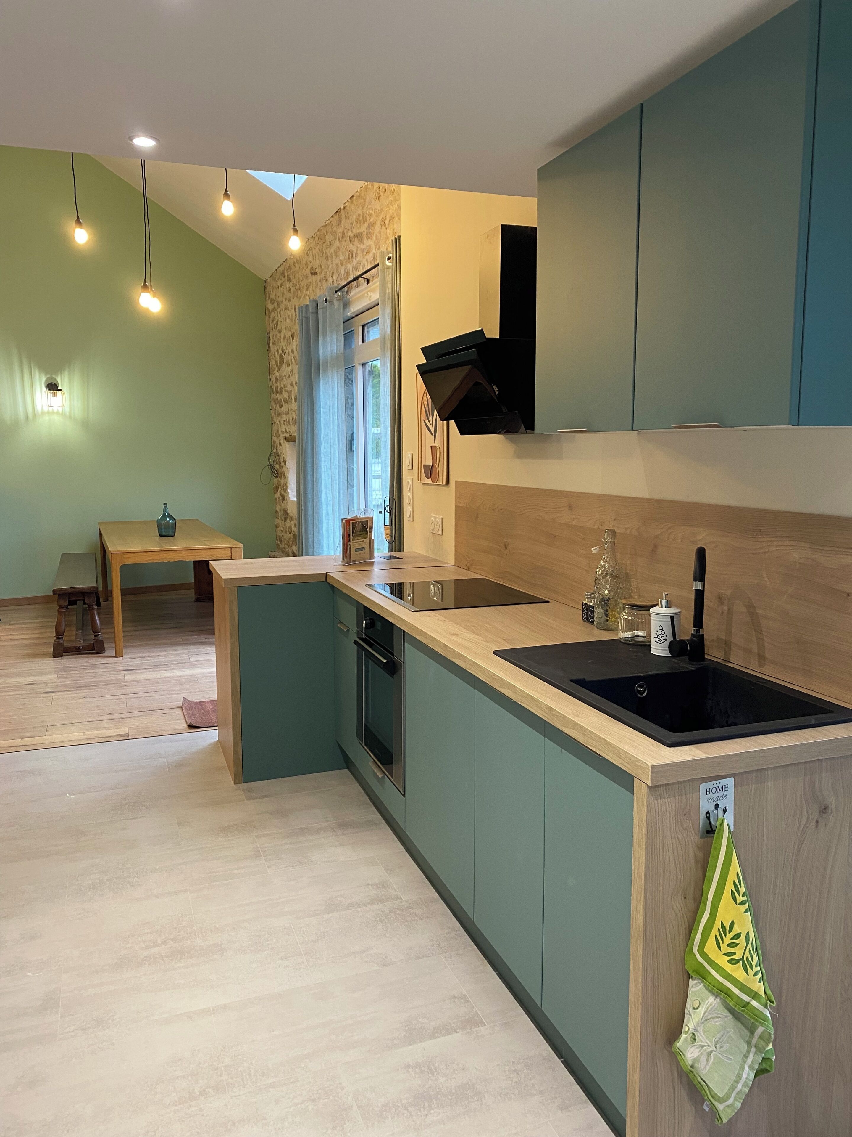 A modern kitchen with a built-in oven, a sink, and a wooden countertop. There is a dining table and chairs in the background.