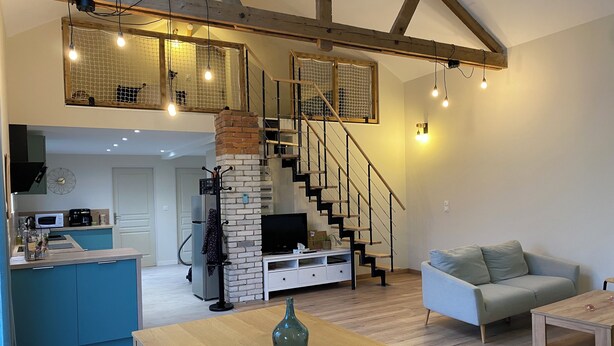 Un vaste espace de vie agrémenté d’un escalier en bois, une cuisine équipée d’appareils modernes et un coin salon confortable.