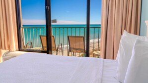 Una camera d'albergo con un letto, vista sulla spiaggia e due sedie.