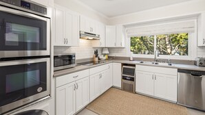 Une cuisine moderne avec des meubles blancs, des appareils en acier inoxydable et une fenêtre donnant sur les arbres.