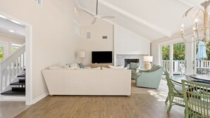 Un vaste espace de vie comprenant un canapé blanc, un téléviseur à écran plat, une cheminée et un coin repas avec une table et des chaises.