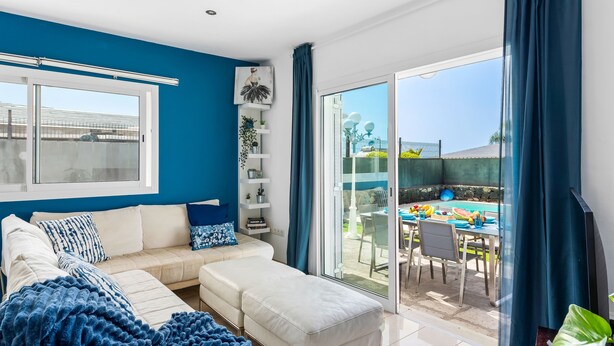 Uma sala de estar moderna com uma parede azul, um sofá branco e uma porta de correr de vidro que dá para uma área de jantar ao ar livre.