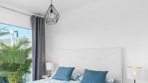 Quarto moderno com cama grande, luminária pendente, mesa de cabeceira com abajur e vista para o verde lá fora.