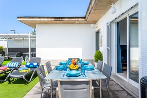 Ein Essbereich im Freien mit einem Tisch für sechs Personen, umgeben von Lounge-Stühlen und einer Glasschiebetür, die auf eine überdachte Terrasse führt.