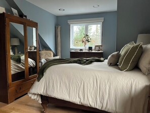 Relax in a serene bedroom with a large bed and stylish armoire, offering a peaceful retreat with a view of lush greenery.