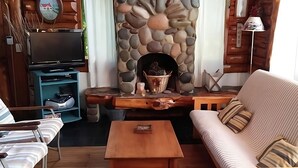 A cozy living room with a stone fireplace, a television, and comfortable seating. - Willow log cabin (Mar de las Pampas)