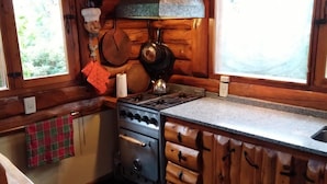 A kitchen with a gas stove, wooden cabinets, and a window with a view of greenery. - Willow log cabin (Mar de las Pampas)