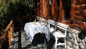 A rustic wooden cabin with a stone foundation, a white bench, and a table set with a bottle and a glass. - Willow log cabin (Mar de las Pampas)