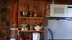 A kitchen with wooden cabinets, a microwave, a refrigerator, and various kitchen appliances on the counter. - Willow log cabin (Mar de las Pampas)