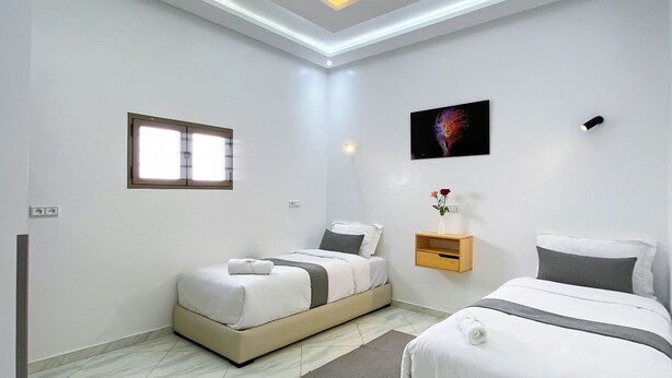 A modern hotel room with two beds, a flat-screen TV, a small window, and a ceiling light fixture. - Residence America (Dakhla)
