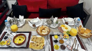 A breakfast table with various dishes, including eggs, bread, and beverages, set on a white tablecloth in a room with red and black upholstered seating. - Residence America (Dakhla)
