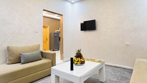 A modern living room with a sofa, a coffee table with fruit, and a flat-screen TV. - Residence America (Dakhla)