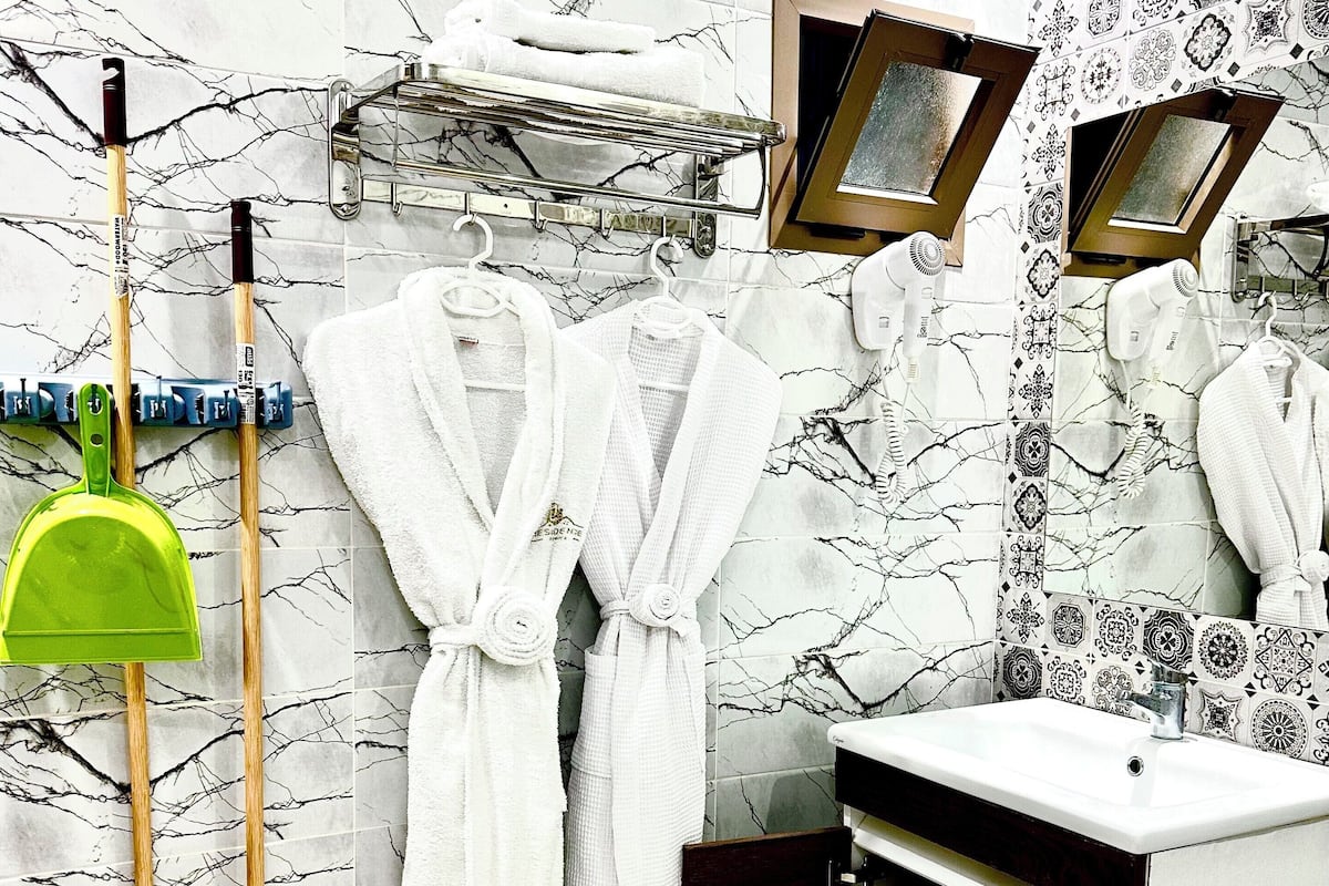 A bathroom with a marble backsplash, a sink, a mirror, and a towel rack with white robes.