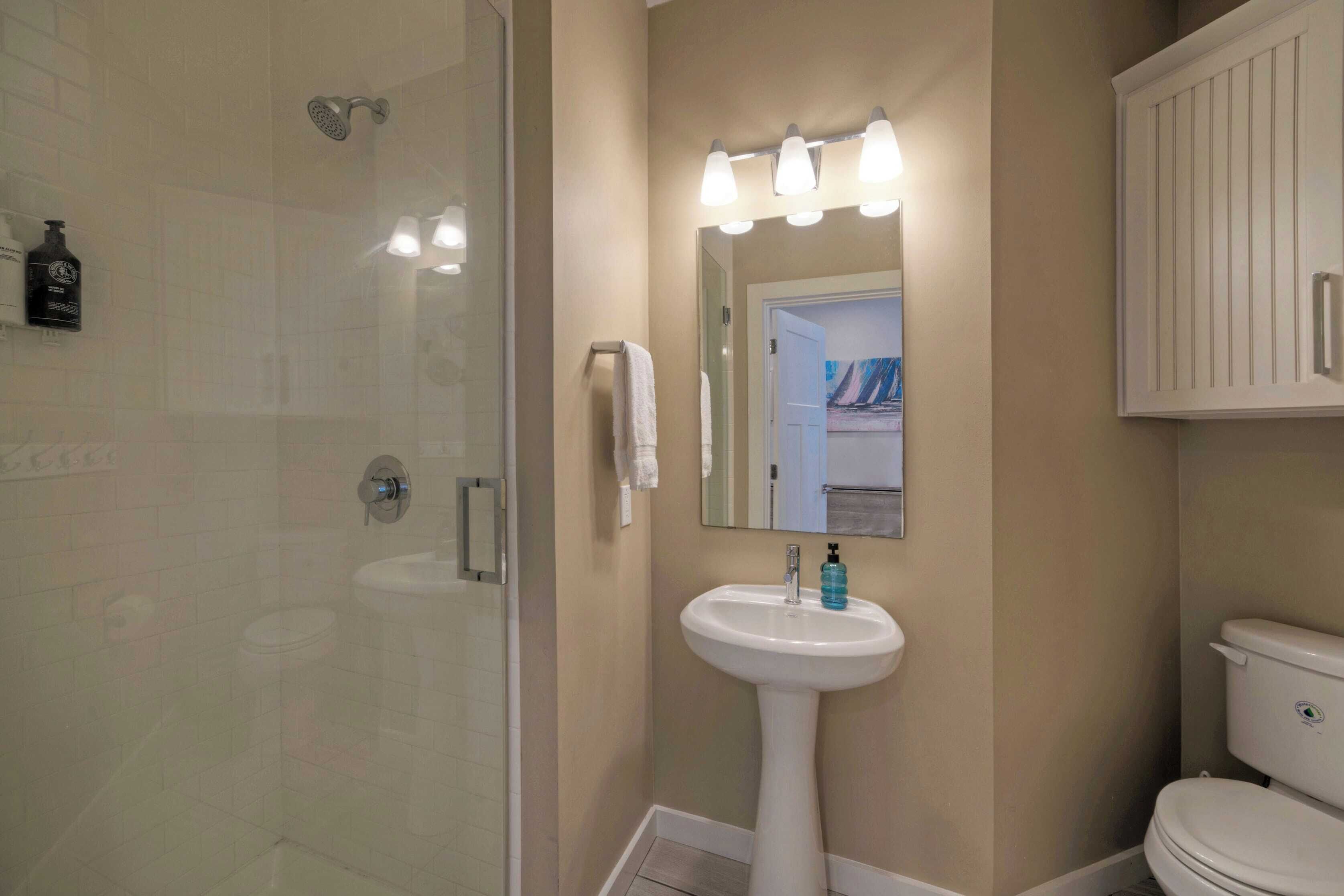 A bathroom with a glass shower enclosure, a pedestal sink, and a toilet.