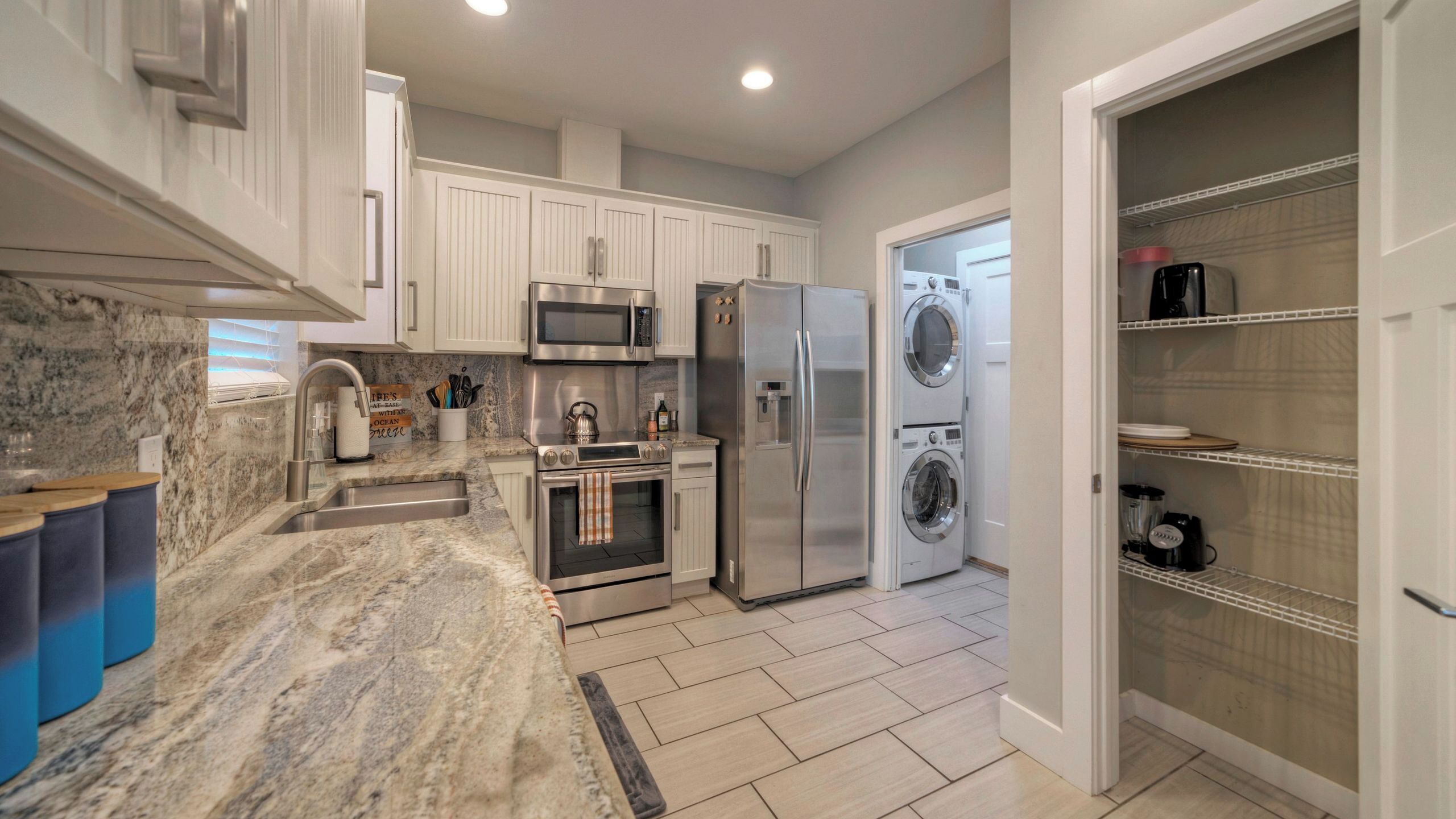 A modern kitchen with white cabinetry, stainless steel appliances, a marble countertop, and a built-in oven.