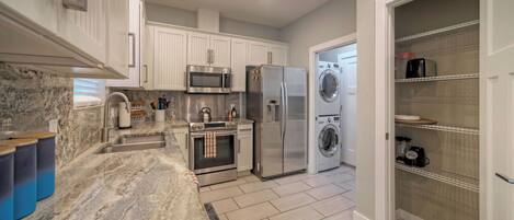 A modern kitchen with white cabinetry, stainless steel appliances, a marble countertop, and a built-in oven.